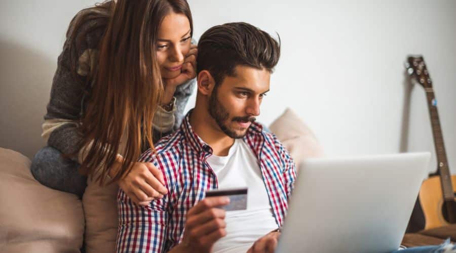 Compre a passagem no momento certo. Casal comprando uma passagem com o cartão de crédito na mão e olhando para o notebook