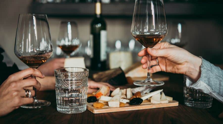 Degustação de vinhos e queijos na Vinícola Cockburn's. Duas mão segurando taças de vinhos brindando e ao fundo um mix de queijos