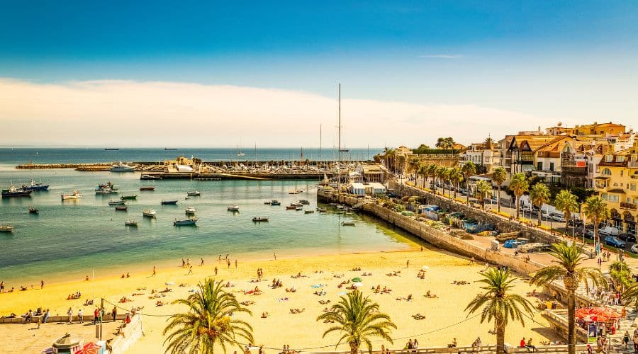 Vista do alto da Praia da Ribeira em Cascais. Com barcos ancorados e com o mar ao fundo no final do dia