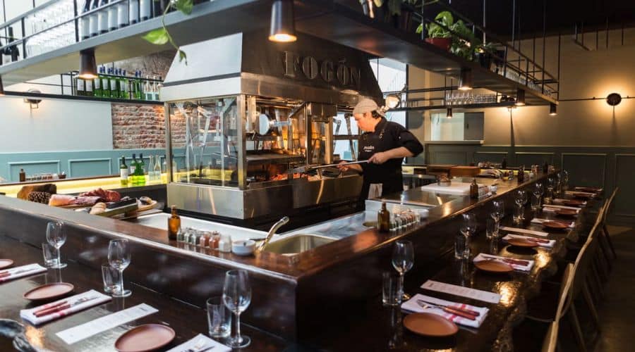 Fogón Asado. Parrillero em frente a parrilla modelo argentino e um balcão que fica em volta da parrilla onde é servidos o jantar
