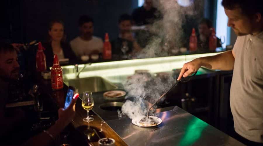Restaurante Fogón Asado. Chefe com uma chapa quente servindo uma pessoa que está impressionada com o corte de carne que está servindo.