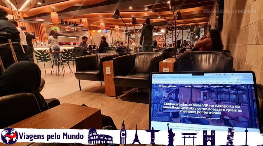 Sala VIP Advantage. Poltronas confortáveis com pessoas em pé se servindo no buffet e um notebook aberto com o site Viagens pelo Mundo aberto.
