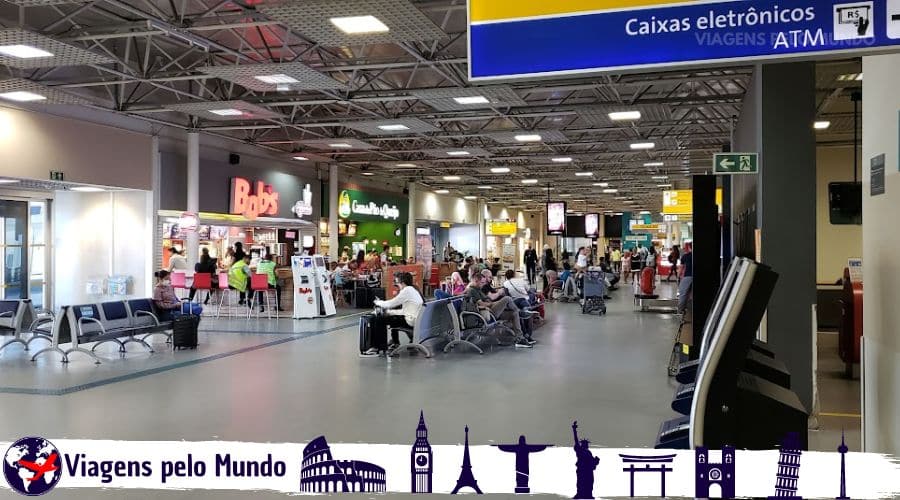 Terminal 1 do Aeroporto de Guarulhos. Lojas e lanchonetes com banco com passageiros sentados