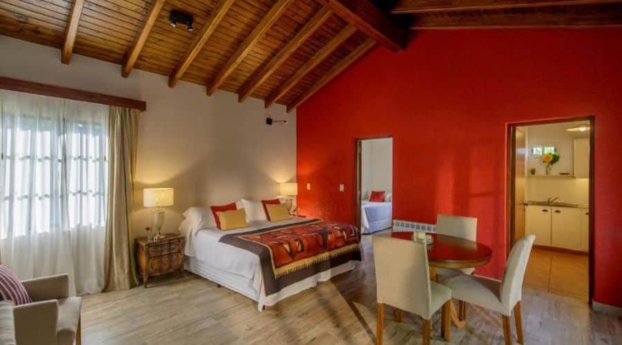 Posada Verde Oliva: quarto espaçoso com paredes vermelhas vibrantes, teto de madeira e uma grande janela. A decoração inclui uma cama de casal com cobertura estampada e móveis rústicos, além de uma área de jantar com mesa e cadeiras, proporcionando um ambiente confortável e acolhedor.