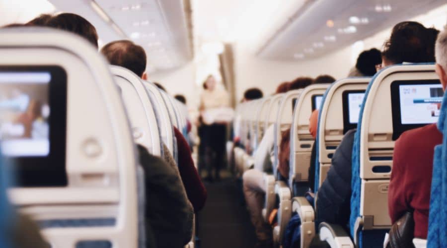Passageiros sentados no avião e no corredor a comissária passando verificando antes do avião decolar.