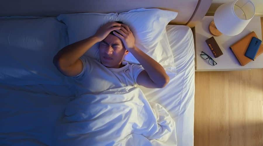 Homem deitado na cama com dificuldade de dormir com a mão na cabeça 